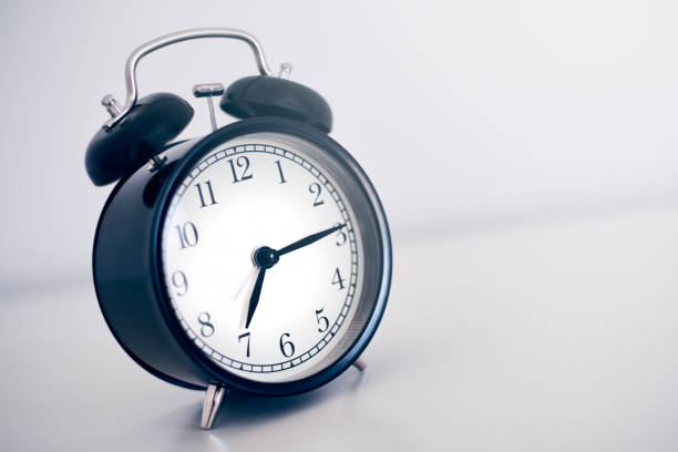 A beautiful black vintage alarm clock with bells and hands indicating 7 am, isolated on white background and with sunlight