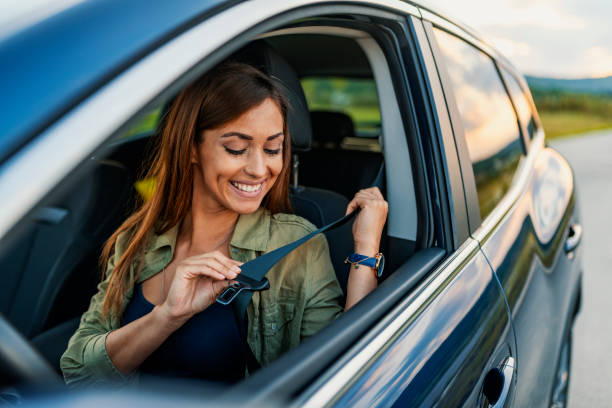 Photo of a business woman sitting in a car putting on her seat belt Young attractive woman sitting on car seat and fastening seat belt, car safety concept. Photo of beautiful young woman fastens a seat belt in the car - outdoors. Brown hair woman fastening seat belt in the car, safety concept. Business lady, Caucasian woman driver fastening car seat belt while sitting behind the wheel car. Safe driving concept. Selective focus, copy space driving stock pictures, royalty-free photos & images