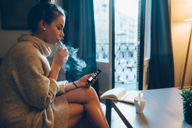 Online banking from smartphone Young girl at home smoking electronic cigarette and online banking on mobile phone vape stock pictures, royalty-free photos & images