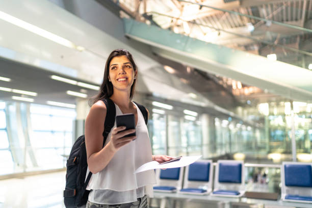 istock Woman holding cellphone and airplane ticket inside an airplane terminal 1163606038