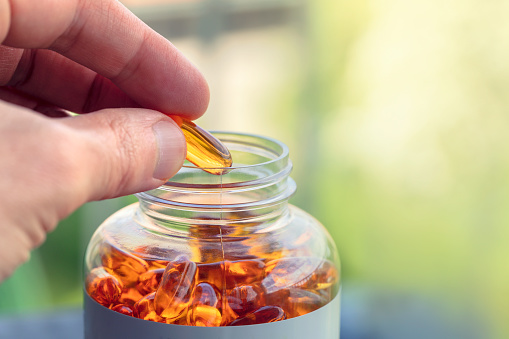 Person taking a fish oil capsule from a jar.
