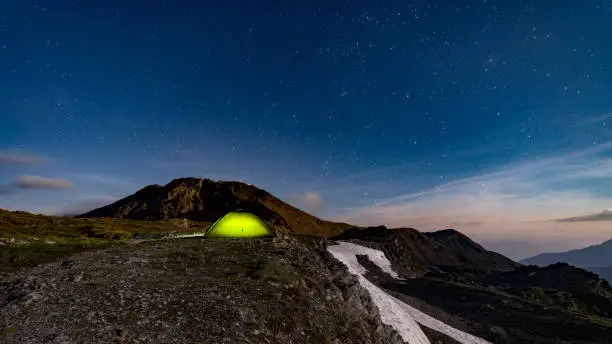 Photo of Panorama with illuminated green tent under starry night - fog rolling over mountains