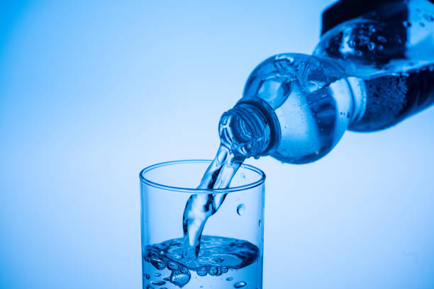 istock water pouring from plastic bottle in glass on blue background with copy space 1163615474
