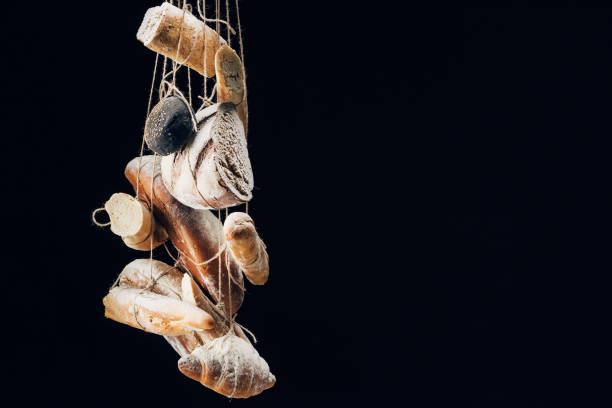 fresh baked bread, baguettes and croissant with flour hanging on ropes isolated on black with copy space