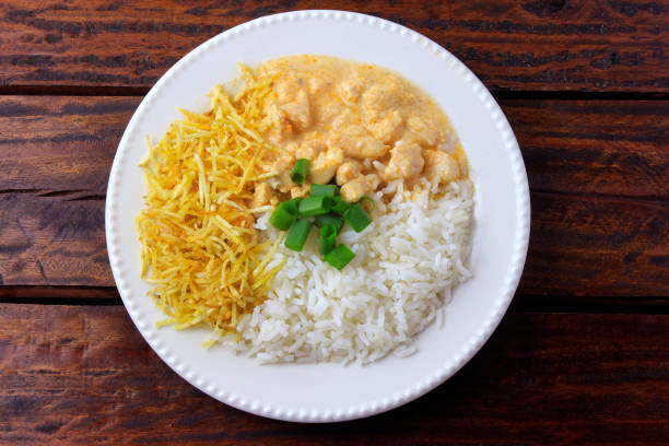 Chicken stroganoff, is a dish originating from Russian cuisine that in Brazil is composed of sour cream with tomato extract, rice and potato chips, on rustic wooden table. Top view. stock photo