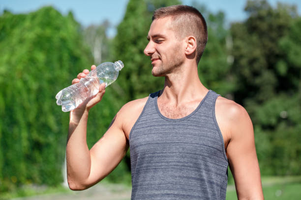istock Healthy Lifestyle. Man practicing yoga outdoors standing drinking water happy side view 1163630408