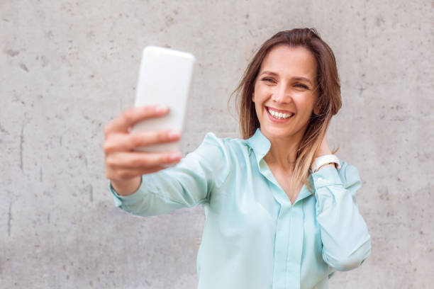 istock Young woman standing isolated on wall taking selfie on smartphone looking camera playful 1163630782