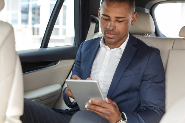 istock Young businessman sitting on back seat in car browsing digital tablet concentrated 1163630997