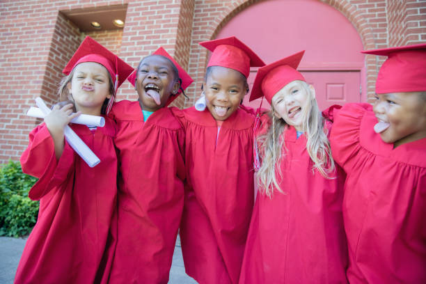 istock Silly preschool graduates make a funny face while posing for photo outside school while wearing caps and gowns 1163631168