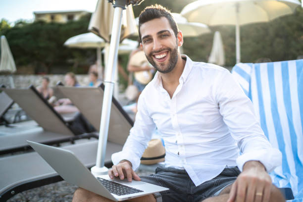 istock Man at swimming pool area using laptop during vacations 1163631898