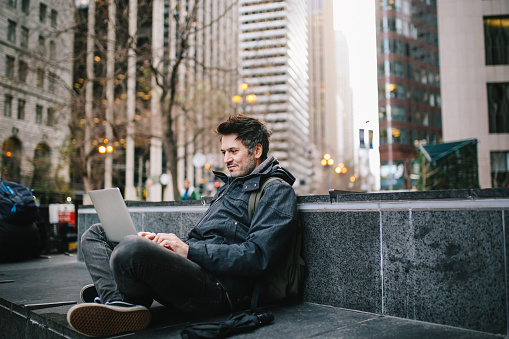 Young IT professional sitting outdoors, finishing work on the laptop, in San Francisco, California.