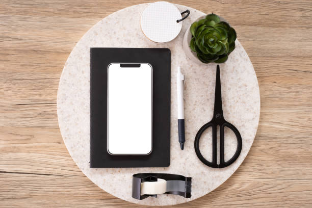 istock mobile mock up on office desk table top view with stationery,notebook,plant on wooden table background.smart phone screen for display of design.business object flat lay.clipping path device template. 1163645311