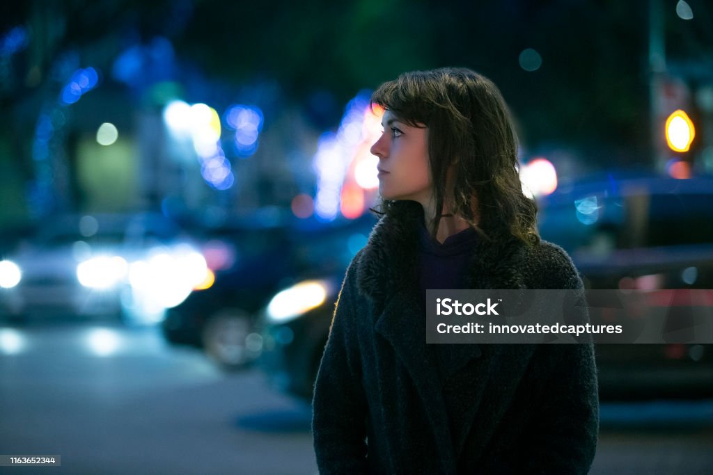Woman Walking At Night in the City Caucasian pedestrian woman walking the street at night in the city with moving cars in the background.  She looks nervous or unsure like a lost tourist or afraid of commuting alone. Night Stock Photo