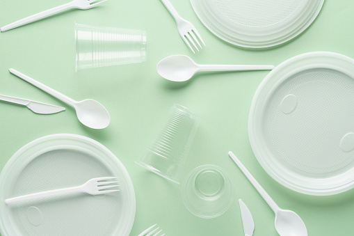 Various white plastic disposable tableware on green background. Creative flat lay.