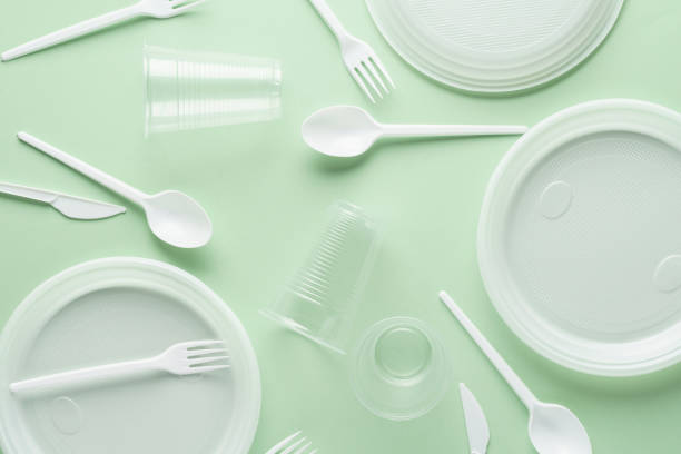 Various white plastic disposable tableware on green background. Various white plastic disposable tableware on green background. Creative flat lay. disposable stock pictures, royalty-free photos & images