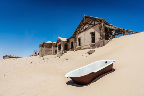 Surreal Scene Abandoned Bathtub on Desert Sand Dune Deserted Ghost Town Surreal Scene in the Namibian Desert. Old broken bathtub on Sand Dune in fronto of abandoned half-timbered old historic buildings in Ghost Town Old Diamond Mine under deep blue desert sky. Kolmanskop, Luderitz, Namibia, Africa. kolmanskop namibia stock pictures, royalty-free photos & images