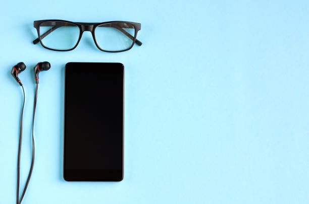 istock Black glasses, cellphone and headphones on blue background composition. 1163664314