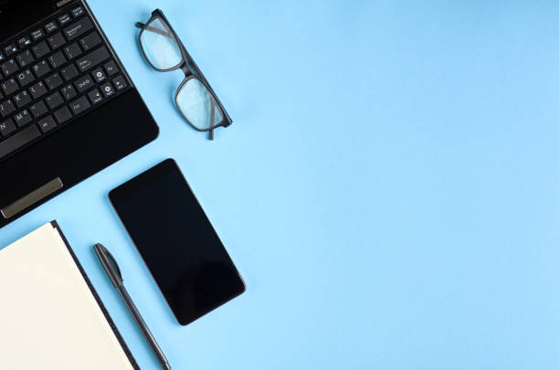 istock Black glasses, cellphone, paper notebook and laptop keyboard on blue background composition. 1163665190