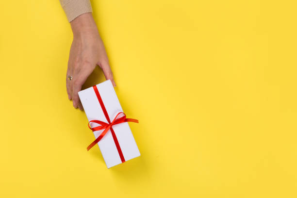 istock Womans hands holding gift or present box on Yellow table top view. Flat lay  for birthday or New Year. 1163665244