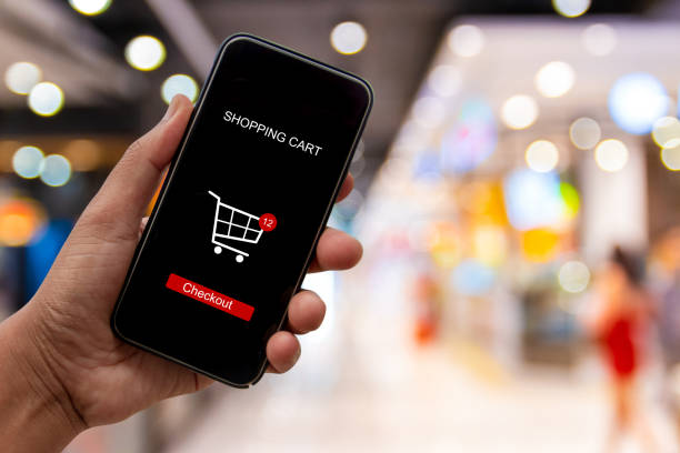 istock Person using smartphone buying and making a payment digitally via application on blur shopping mall background - internet online home shopping concept 1163668649
