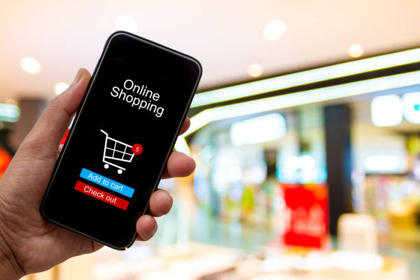 istock Person using smartphone buying and making a payment digitally via application on blur shopping mall background - internet online home shopping concept 1163668663