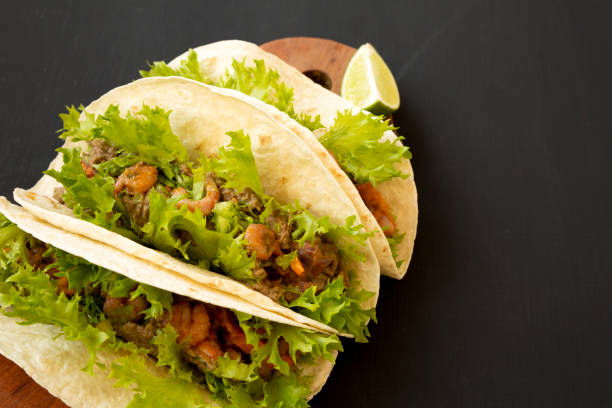 istock Shrimp tacos on a rustic wooden board on a black background, side view. Mexican cuisine. Copy space. 1163669043