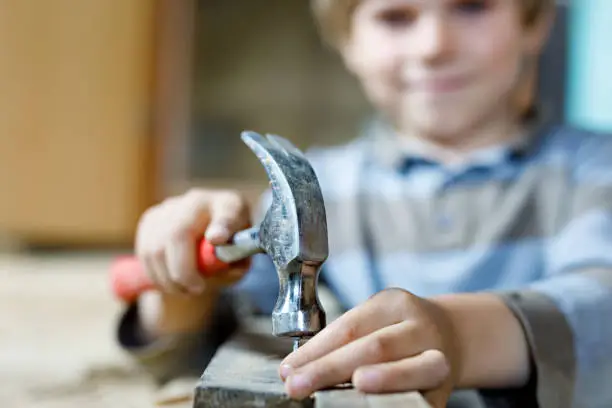 happy little kid boy helping with toy tools on construction site. Funny child of 7 years having fun on building new family home. Kid with nails and hammer. Selective focus on hands and tools