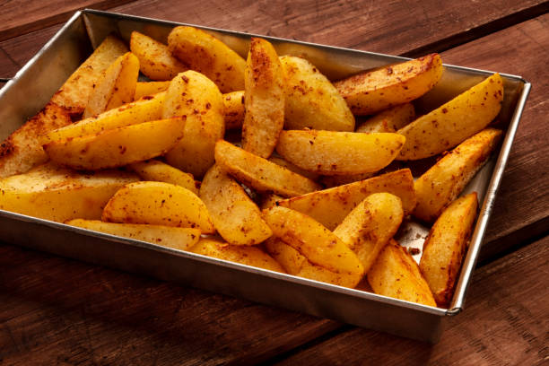 Potato wedges, oven baked, in a baking tray on a rustic background