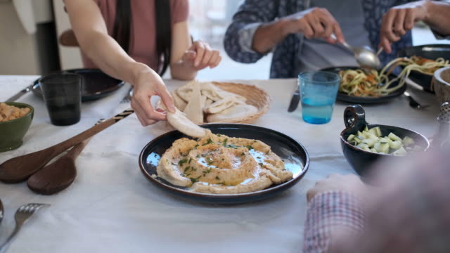 Friends enjoying a vegan meal, close-up of hands reaching for the humus.