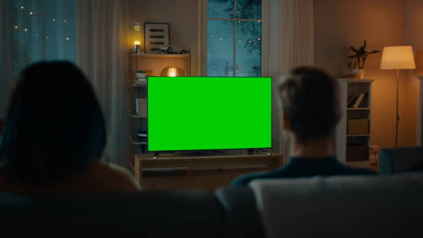 pareja mira tv de pantalla de mock-up verde mientras se sienta en un sofá en la sala de estar. noche romántica para novio y novia. - greenback fotografías e imágenes de stock