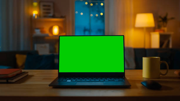 녹색 크로마 키 화면을 보여주는 노트북 컴퓨터는 거실의 책상에 서 있습니다. 따뜻한 조명이켜진 저녁에 배경 아늑한 거실에서. - key house house key green 뉴스 사진 이미지