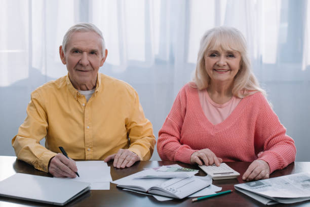 istock senior coupe looking at camera while sitting at table with calculator and counting money 1163676506