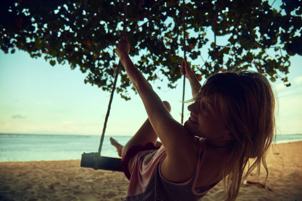istock Young woman swinging on a sandy tropical beach. 1163677983