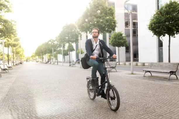 Photo series of a young adult male commuting with electric bicycle through Berlin and doing business at the same time, drinking coffee from reusable coffee cup, listening to podcasts and making business calls.