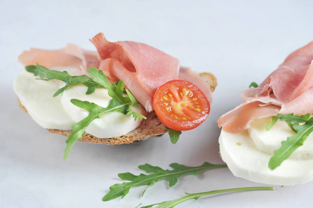 istock Bruschetta with prosciutto and mozzarella. The snack is decorated with arugula and a slice of tomato. 1163679221