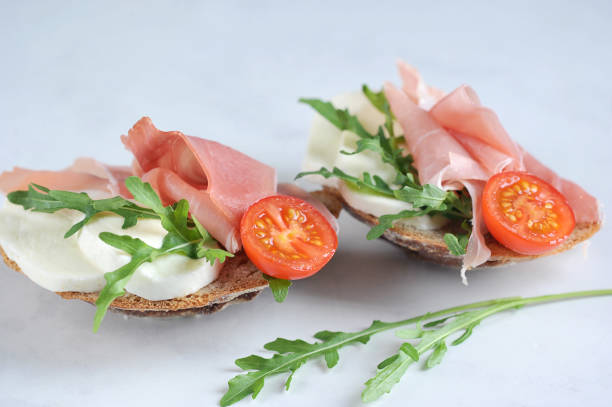 istock Bruschetta with prosciutto and mozzarella. The snack is decorated with arugula and a slice of tomato. 1163681395