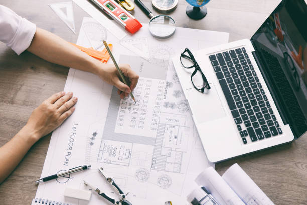 istock Architect hands working on blueprint plans  with  a pencil,  a ruler, calculator, smartphone, laptop and engineering tools 1163686964