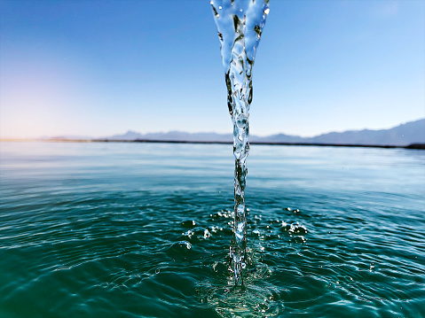 Behind low view point of flowing falling into a dam full to the brim with clear blue water in the Namibian desert with mountains behind and clear blue sky Namibia Africa.  Living water giving life to all.