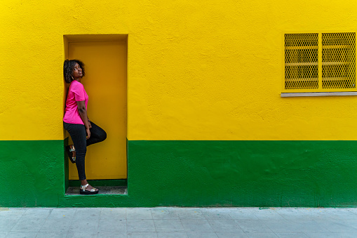 Beautiful young woman in pink t-shirt standing at a yellow and green doorway.