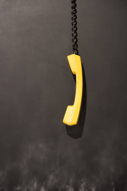 Old yellow handset with black wire hanging on dark background