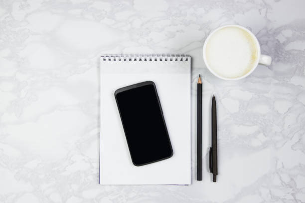 istock Workplace with telephone, notepad, writing pen and a cup of coffee on a marble table. Top view, flat lay, copy space 1163691914
