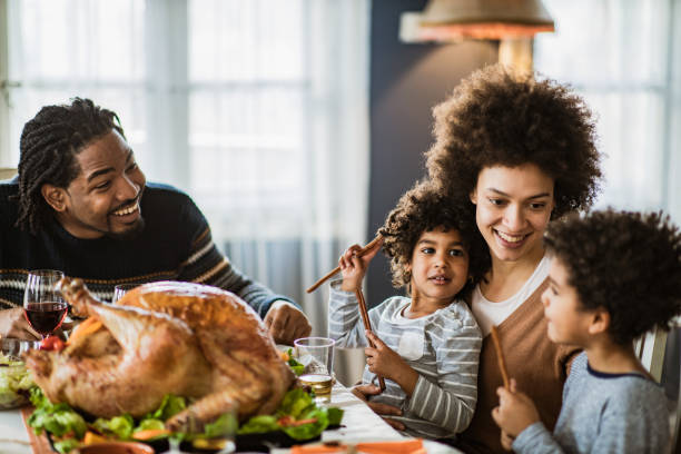 Happy black family talking during Thanksgiving meal at dining table. Happy African American family communicating while having Thanksgiving lunch in dining room. dining table photos stock pictures, royalty-free photos & images