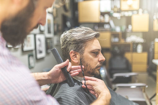 Handsome bearded man having his hair cut by hairdresser at the barbershop