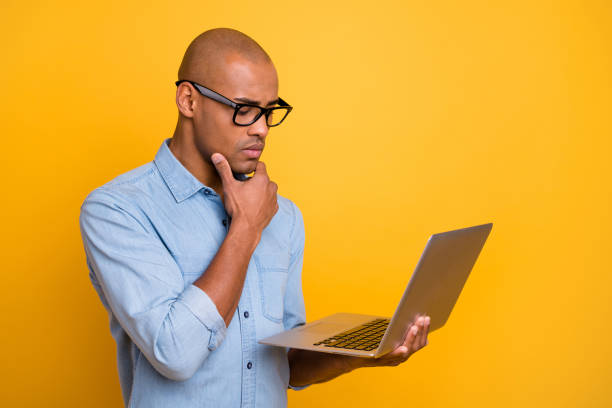 Photo of dark skin guy searching website notebook attentive hand chin wear specs jeans denim shirt isolated bright yellow background Photo of dark skin guy searching website notebook attentive hand chin wear specs, jeans denim shirt isolated bright yellow background deep pick stock pictures, royalty-free photos & images