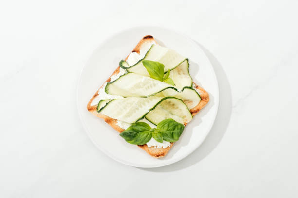 istock Top view of toast with sliced cucumber and basil on plate on white surface 1163696369
