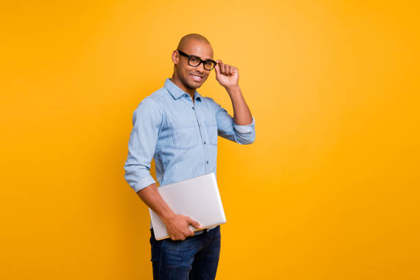 foto de pele escura cara notebook mãos sala de aula jovem professor de escola desgaste especificações jeans denim camisa isolada brilhante fundo amarelo - elegance yellow glasses eyewear - fotografias e filmes do acervo