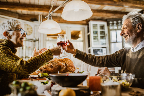 Happy mature couple toasting with wine while having Thanksgiving meal in dining room.