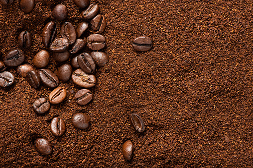 Some coffee beans over ground coffee for coffee theme backgrounds