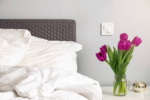 tulipes pourpres restant sur une nuit dans la chambre blanche moderne près du lit. - flower pot vase purple decor photos et images de collection