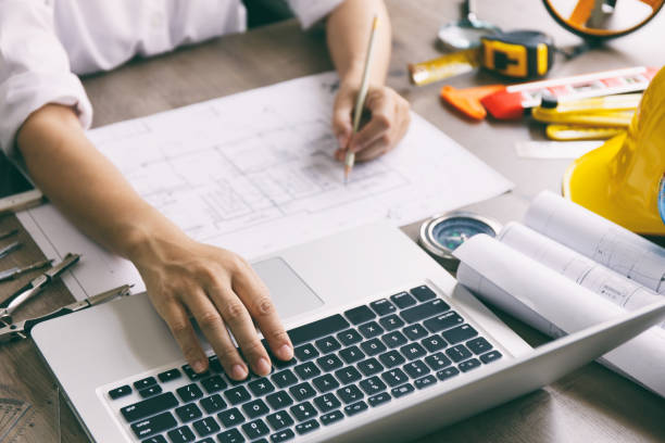 istock Architect hands working on blueprint plans  with  a pencil,  a ruler, calculator, smartphone, laptop and engineering tools 1163704574